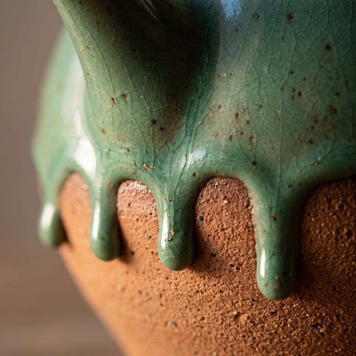 Extreme close-up of thick reactive green glaze dripping over raw unglazed stoneware clay.