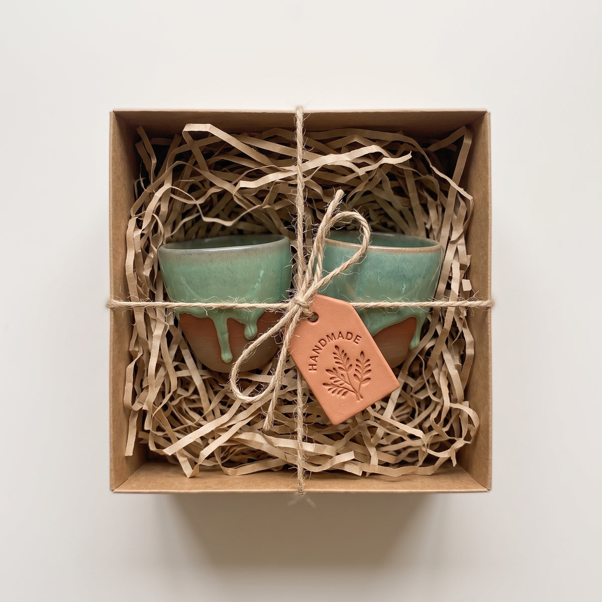 Set of two LyLceramics Olive Sip ceramic cups nestled with natural shred in an artisanal kraft gift box.