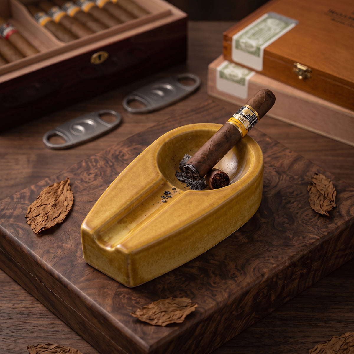 A stylish yellow ceramic cigar ashtray with a single resting cigar on a dark wooden cutting board, surrounded by cigar boxes and accessories.