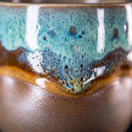 Extreme close-up shot focusing on the tactile texture and unique color variations of the blue dripping reactive glaze on a ceramic shot glass.