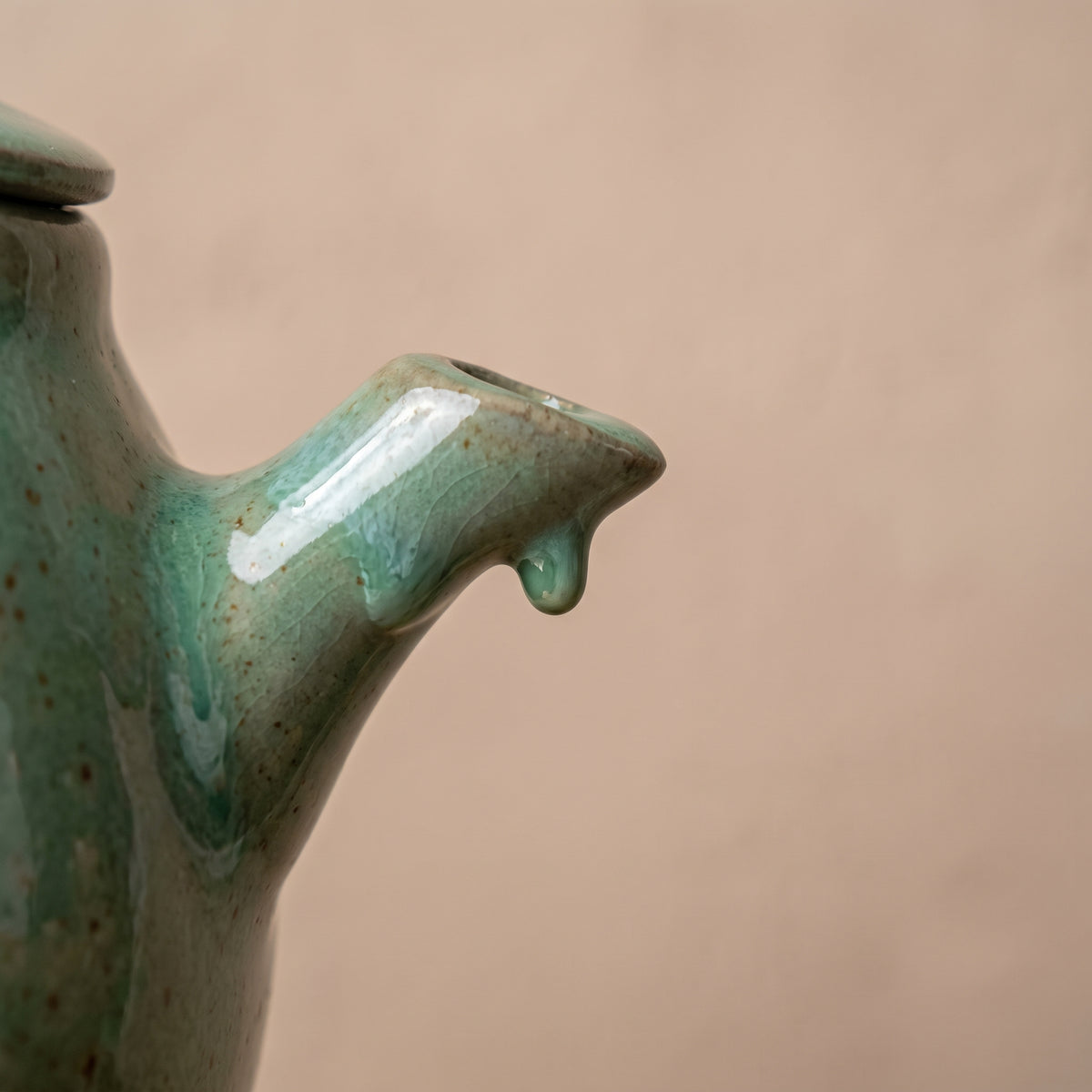 Close-up of ceramic teapot spout showing raw clay texture and dripping reactive green glaze