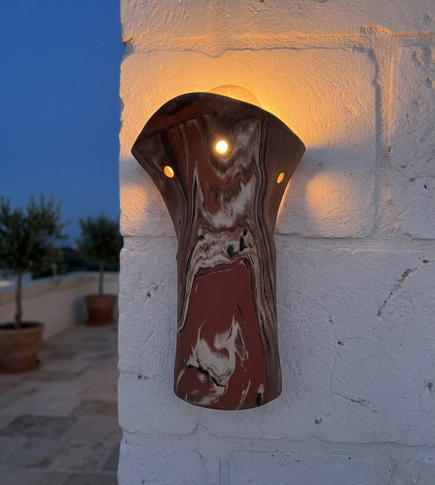 Handcrafted ceramic wall sconce illuminating a rustic white stone exterior building facade