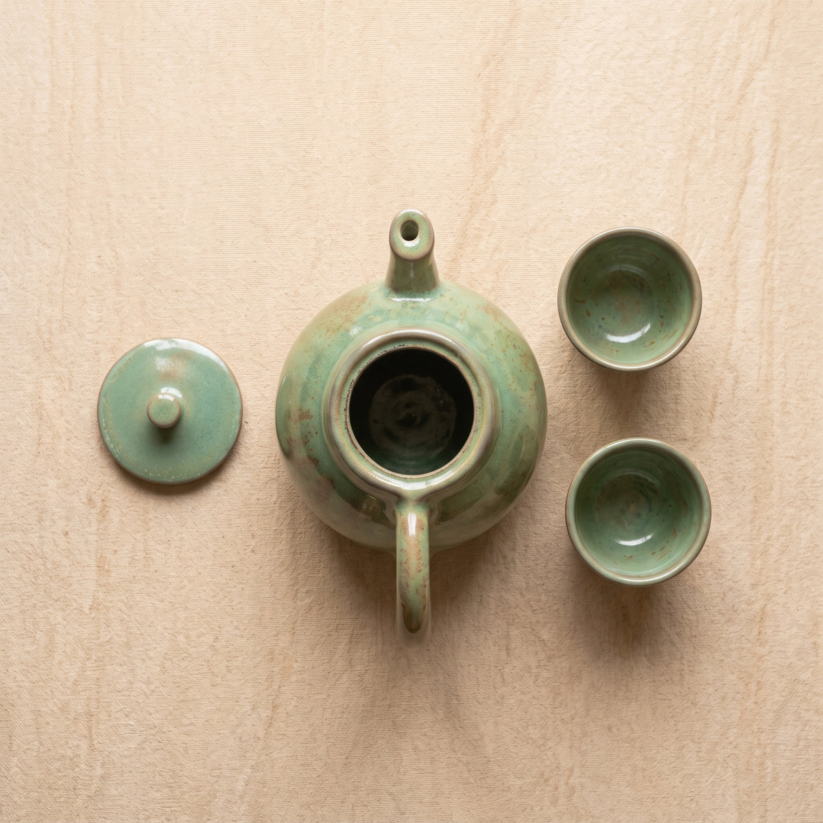 Top-down flat lay view of ceramic tea set with open lid on natural wood surface.