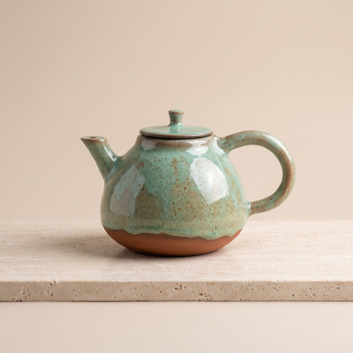 Low angle studio shot of olive stoneware teapot showing round silhouette and handle.