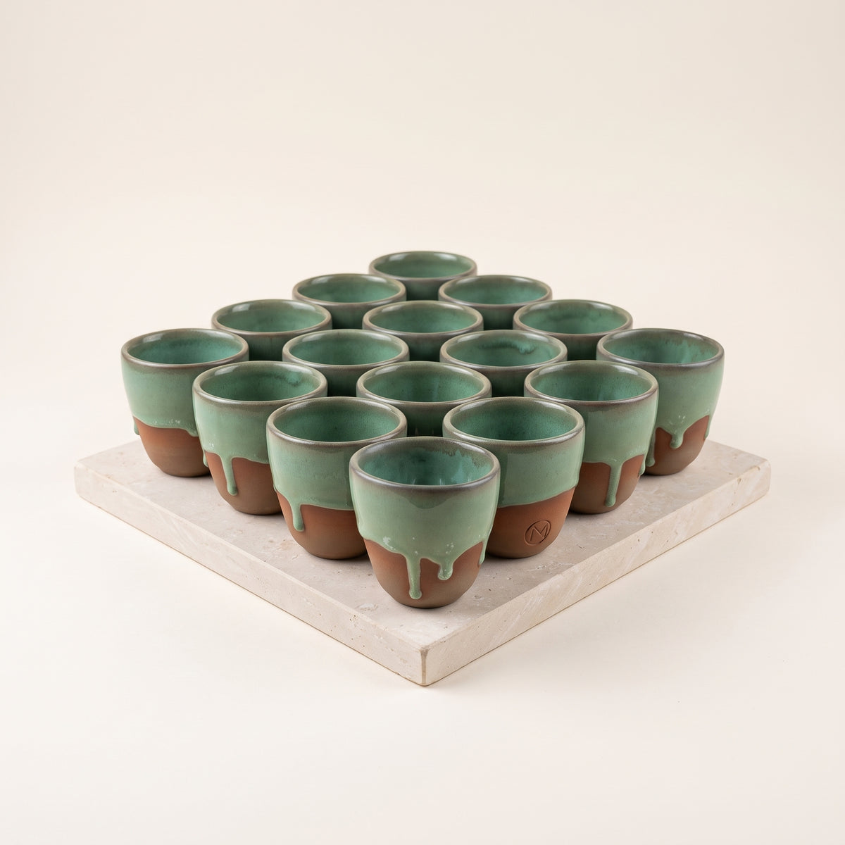 Wholesale batch of handmade olive green ceramic espresso cups displayed on a stone platform.