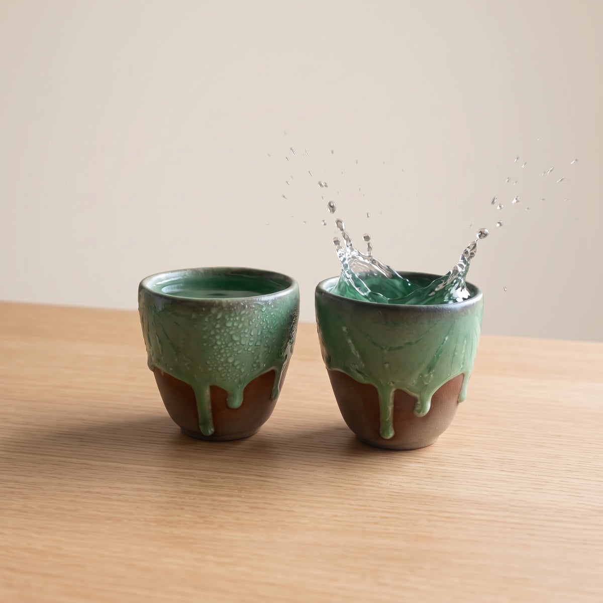 Two LyLceramics Olive Sip stoneware cups with fresh water splashing on a light wooden surface.