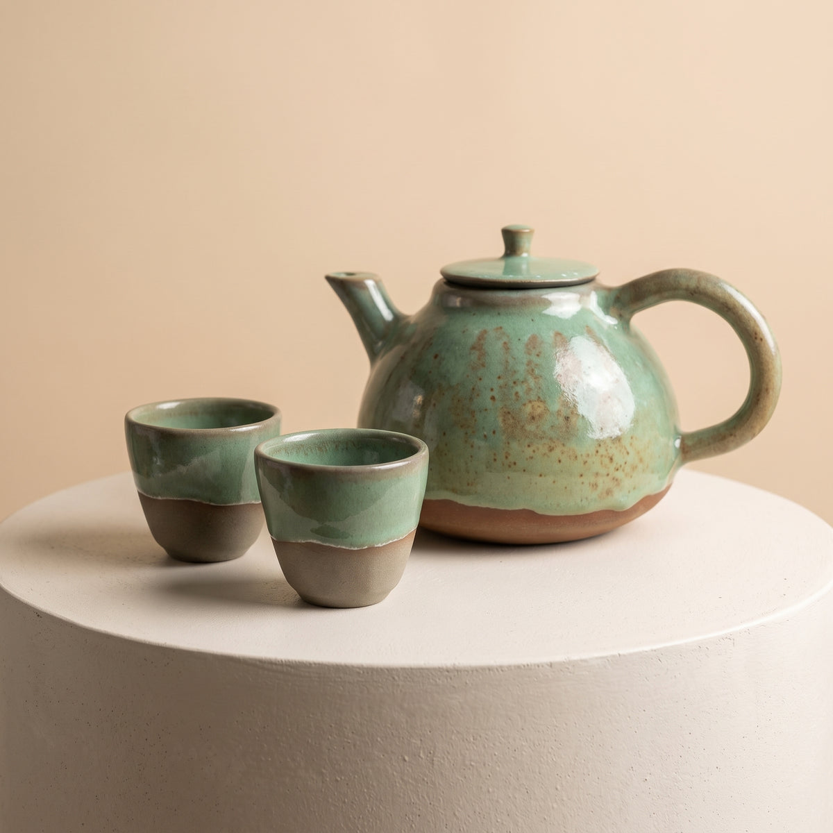 LyLceramics olive stoneware tea set with green glazed teapot and two matching cups on pedestal.