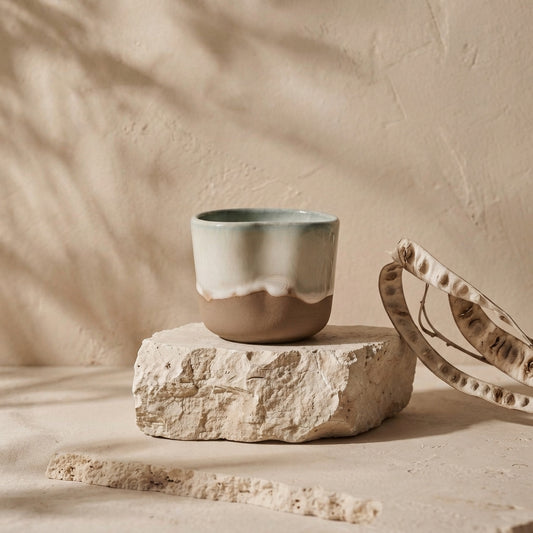 LyLceramics Stone Shot handmade stoneware cup displayed on a natural rough travertine pedestal against a beige background.