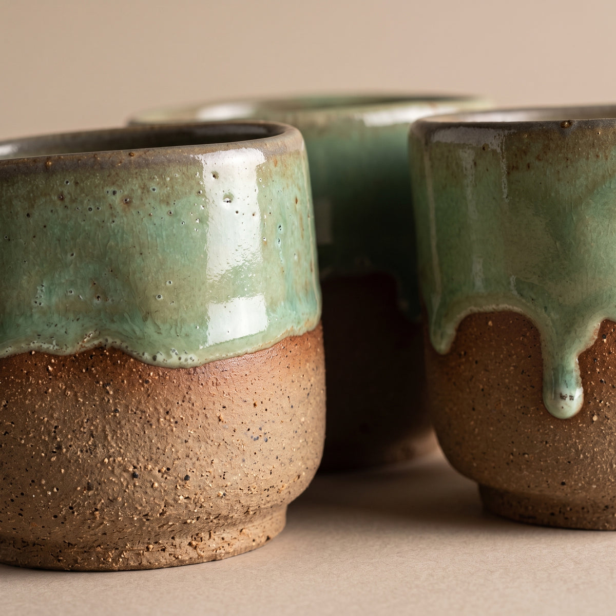 Close-up cluster of LyLceramics Stone Shot cups showcasing individual variations in the olive green drip glaze.