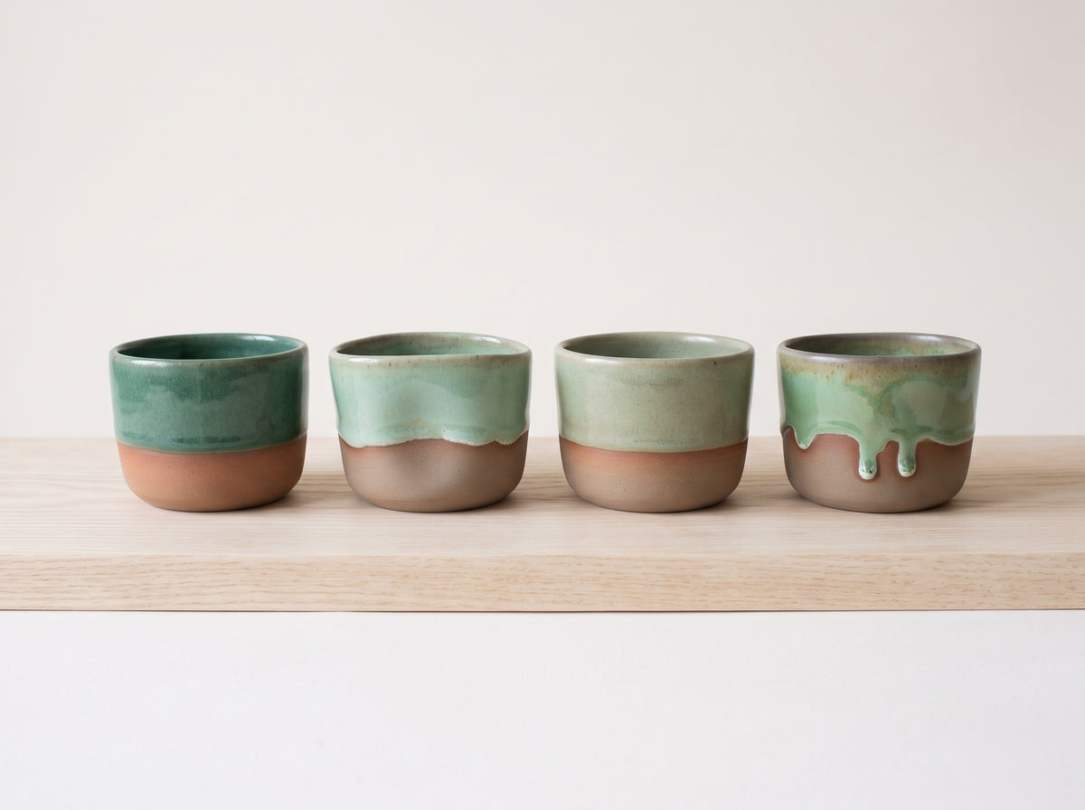 Four handmade stoneware shot glasses lined up neatly along a travertine stone display runner.