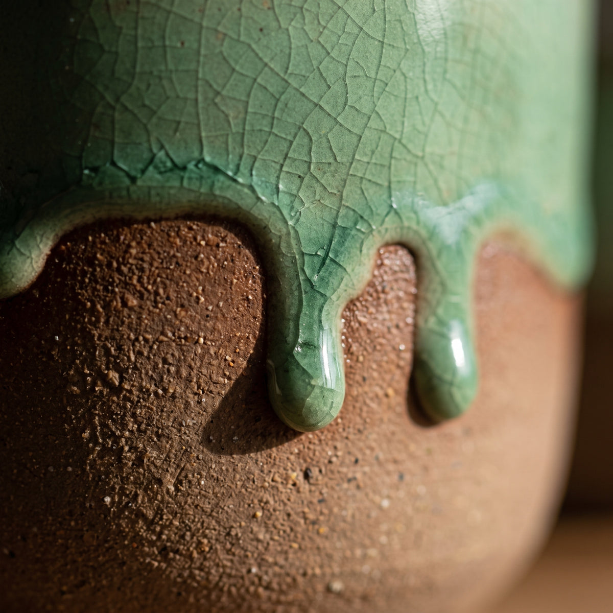 Macro detail showing thick dripping olive green reactive glaze on the raw terracotta stoneware body of a shot cup.