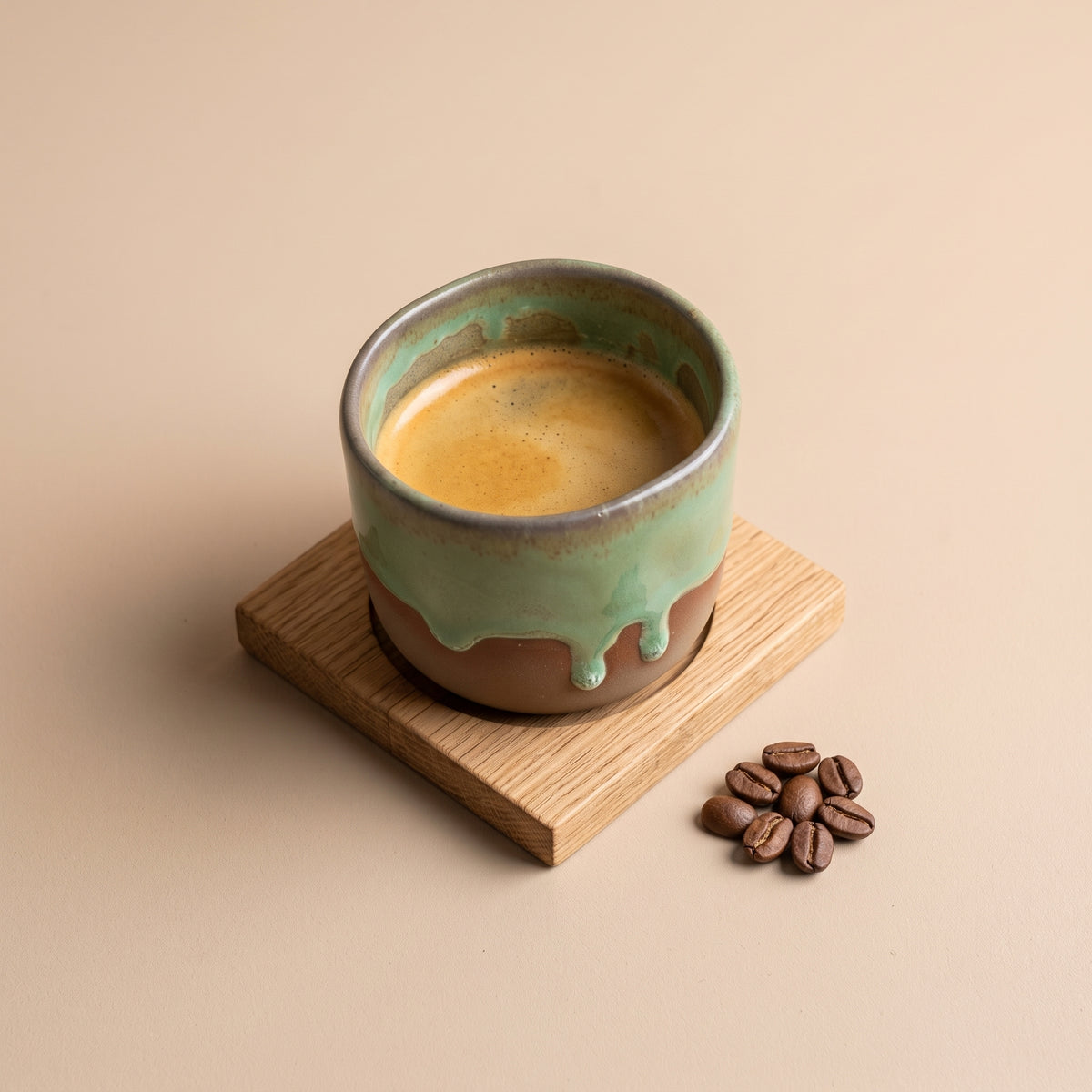 Top-down view of a rich single espresso shot with golden crema in an Olive stoneware shot cup with scattered beans.