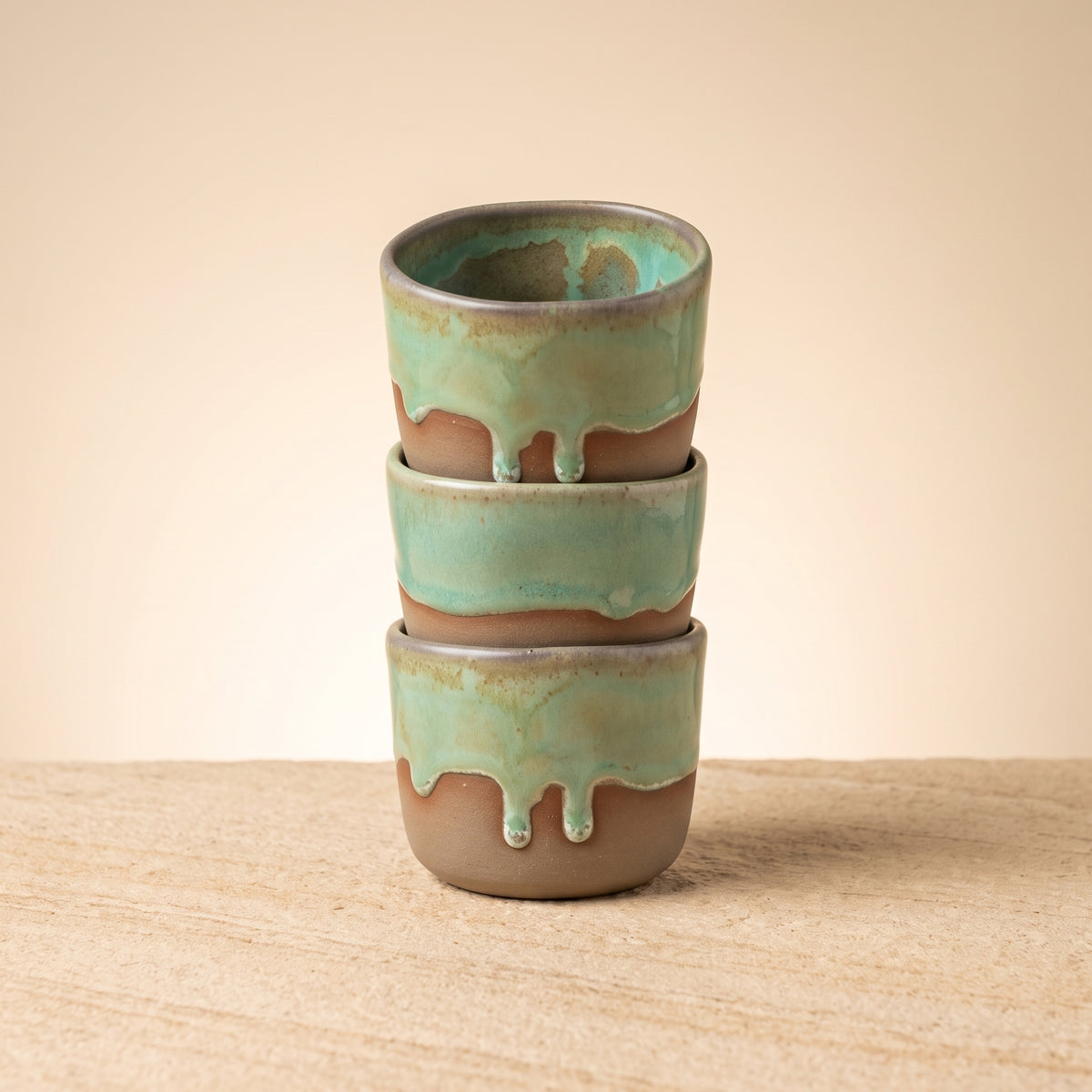 Three LyLceramics Stone Shot handmade ceramic shot cups stacked vertically on a wooden table.