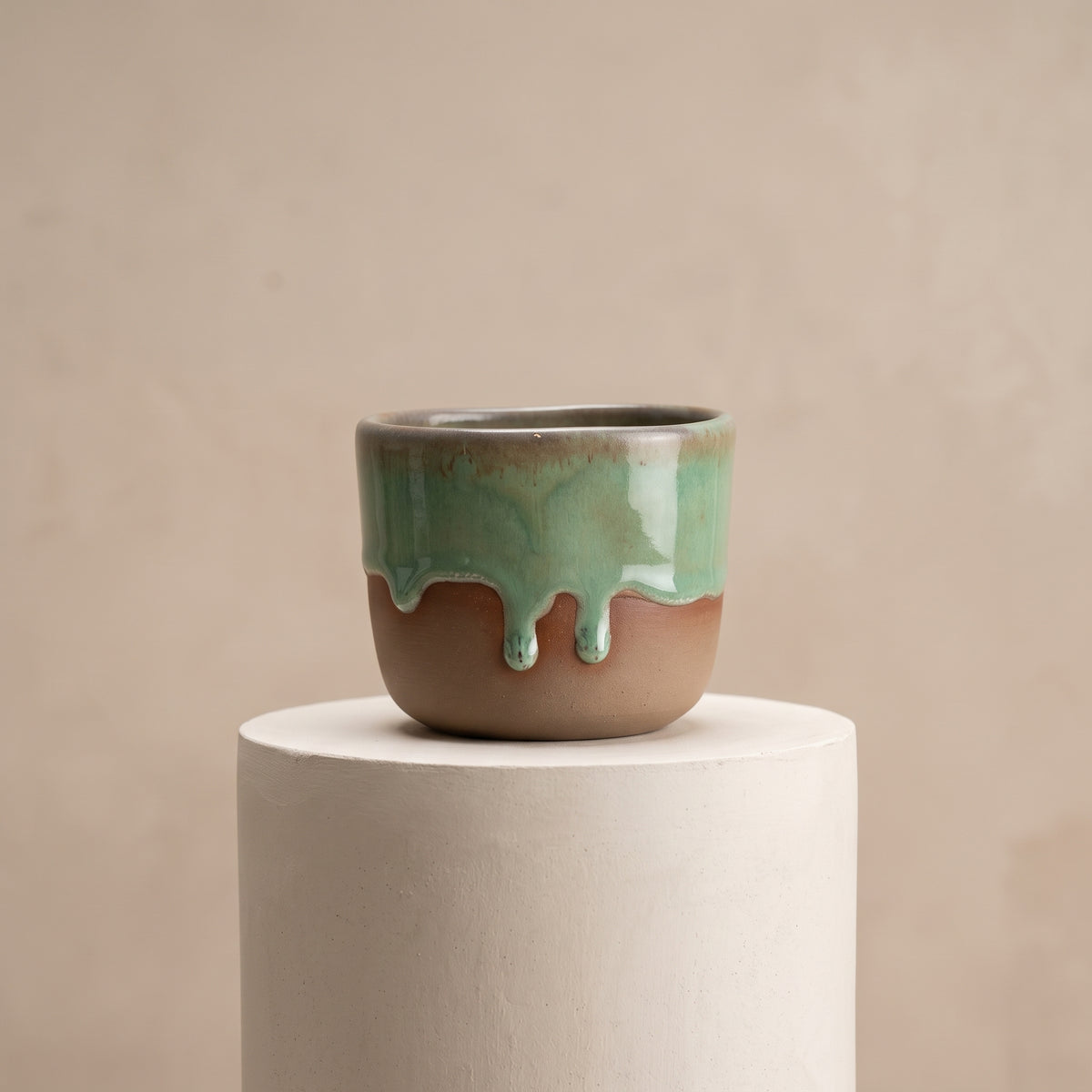 LyLceramics Stone Shot handmade stoneware shot cup with dripping olive green glaze on a white display cylinder.