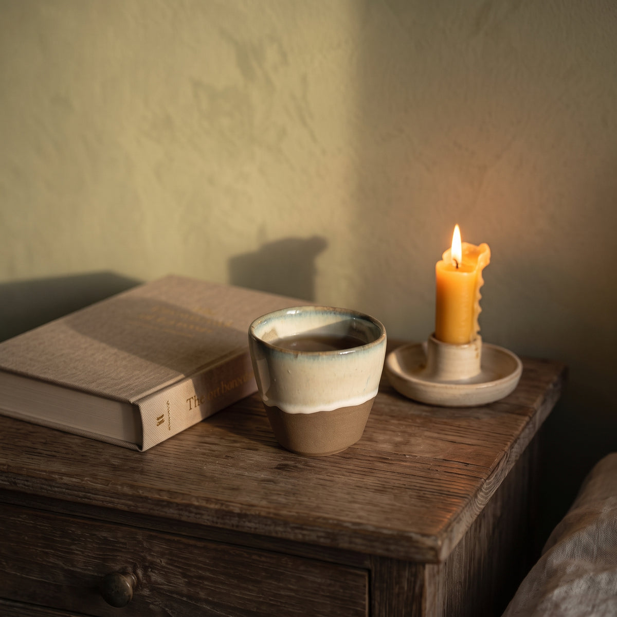 LyLceramics Stone Sip stoneware tumbler placed on a vintage wooden nightstand beside an open book and glowing candle