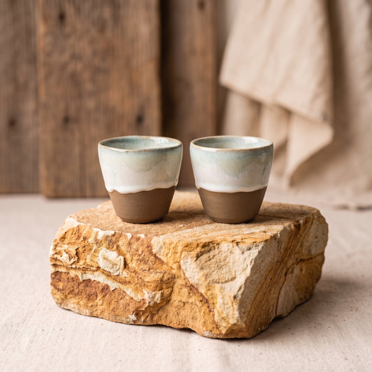Pair of LyLceramics Stone Sip ceramic cups displayed on a rough natural stone pedestal.