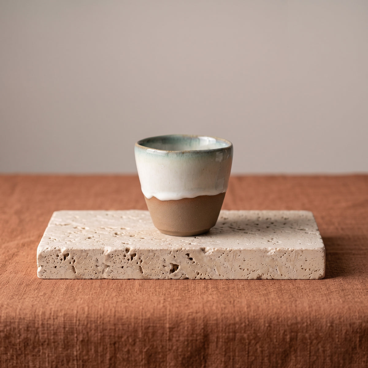 LyLceramics Stone Sip handmade stoneware espresso cup on a raw travertine stone block over terracotta linen.
