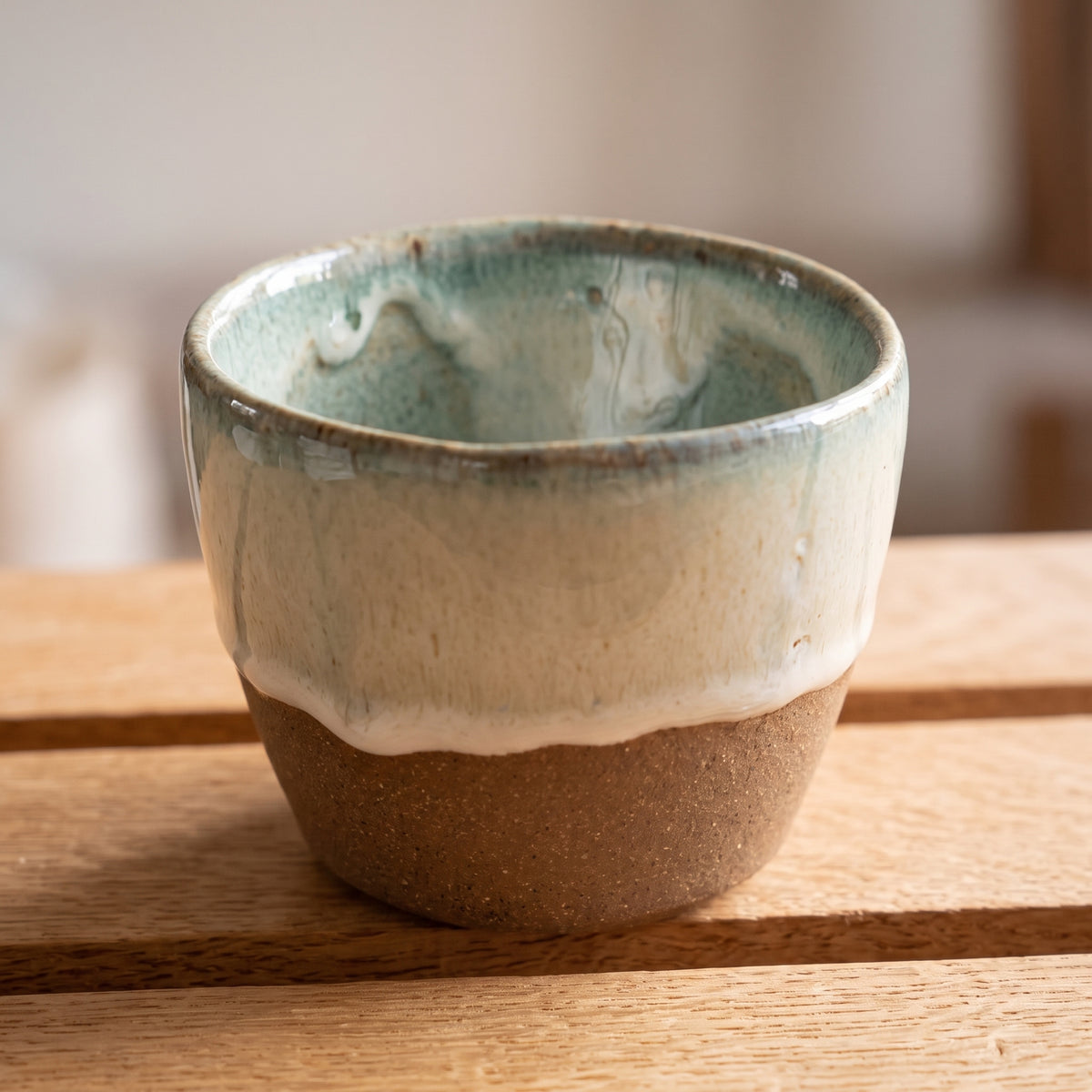 Close-up of LyLceramics Stone Sip ceramic cup showing reactive glaze rim on a natural wooden slatted surface