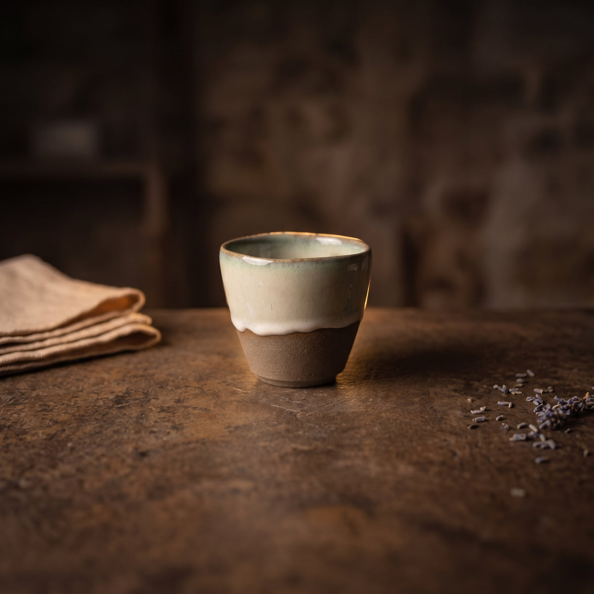 LyLceramics Stone Sip ceramic cup centered on a dark rustic wooden table in warm ambient room light.
