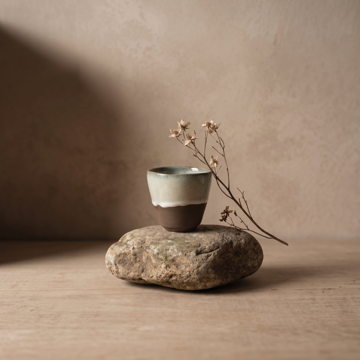 LyLceramics Stone Sip cup perched on a natural river rock with delicate dried botanicals against a warm neutral wall.