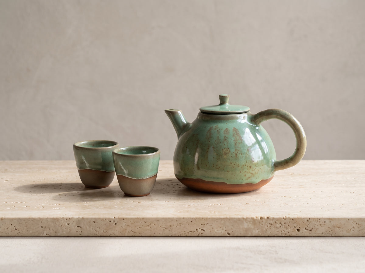 Ceramic olive teapot and cups placed on light wood board, minimalist tea setup