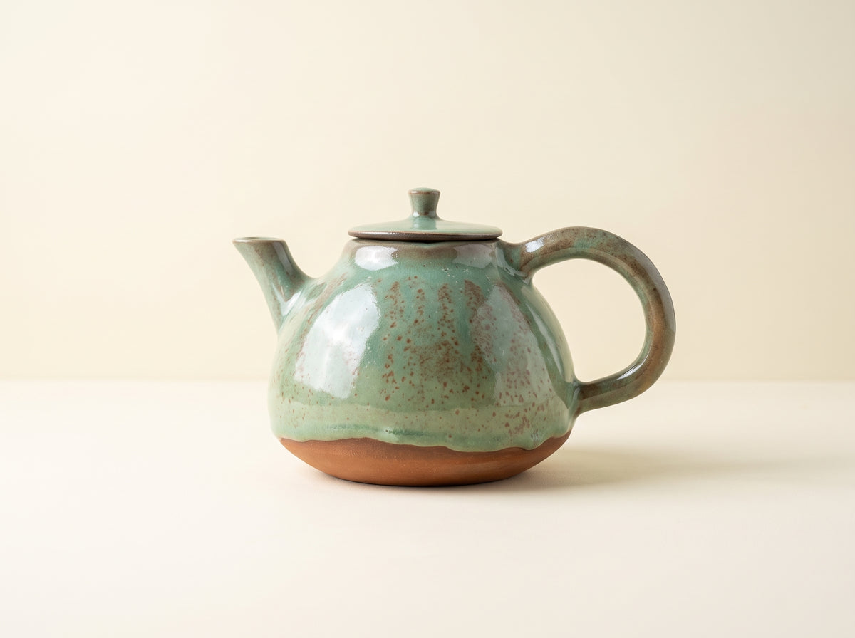 Minimalist olive green stoneware teapot on cream background, side profile.