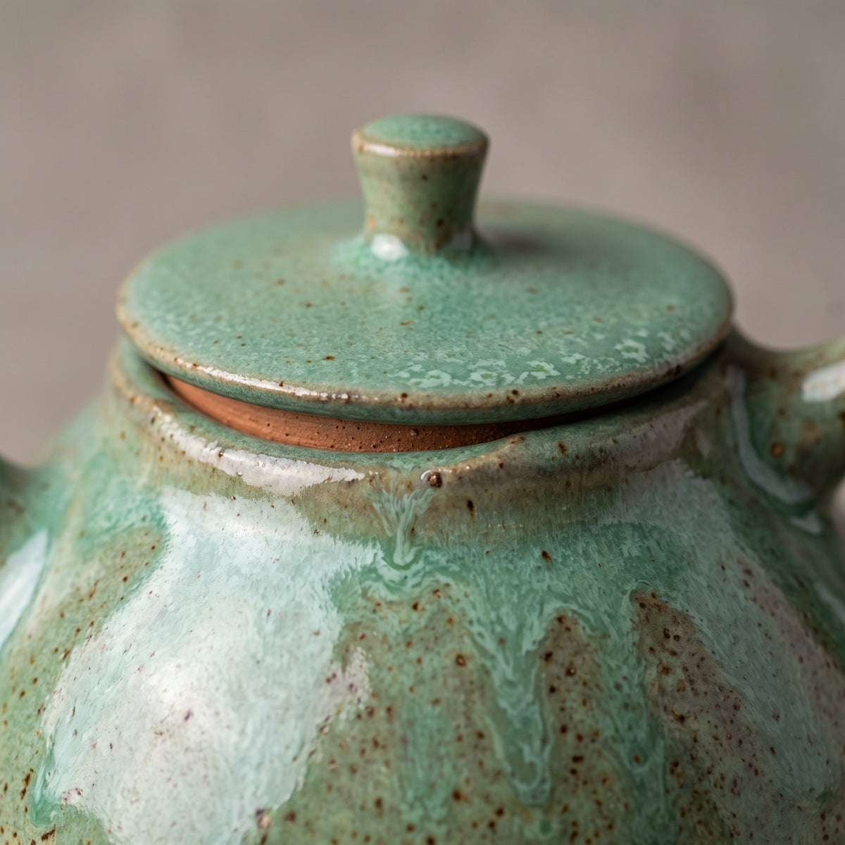 Close-up of olive stoneware teapot lid and shoulder highlighting speckled reactive glaze.