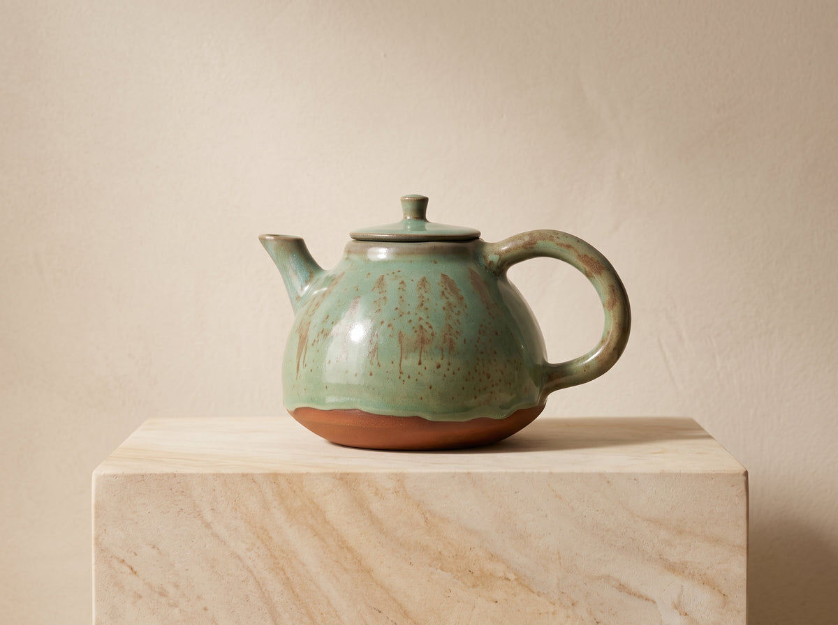 Handmade green ceramic teapot resting on rustic wooden block