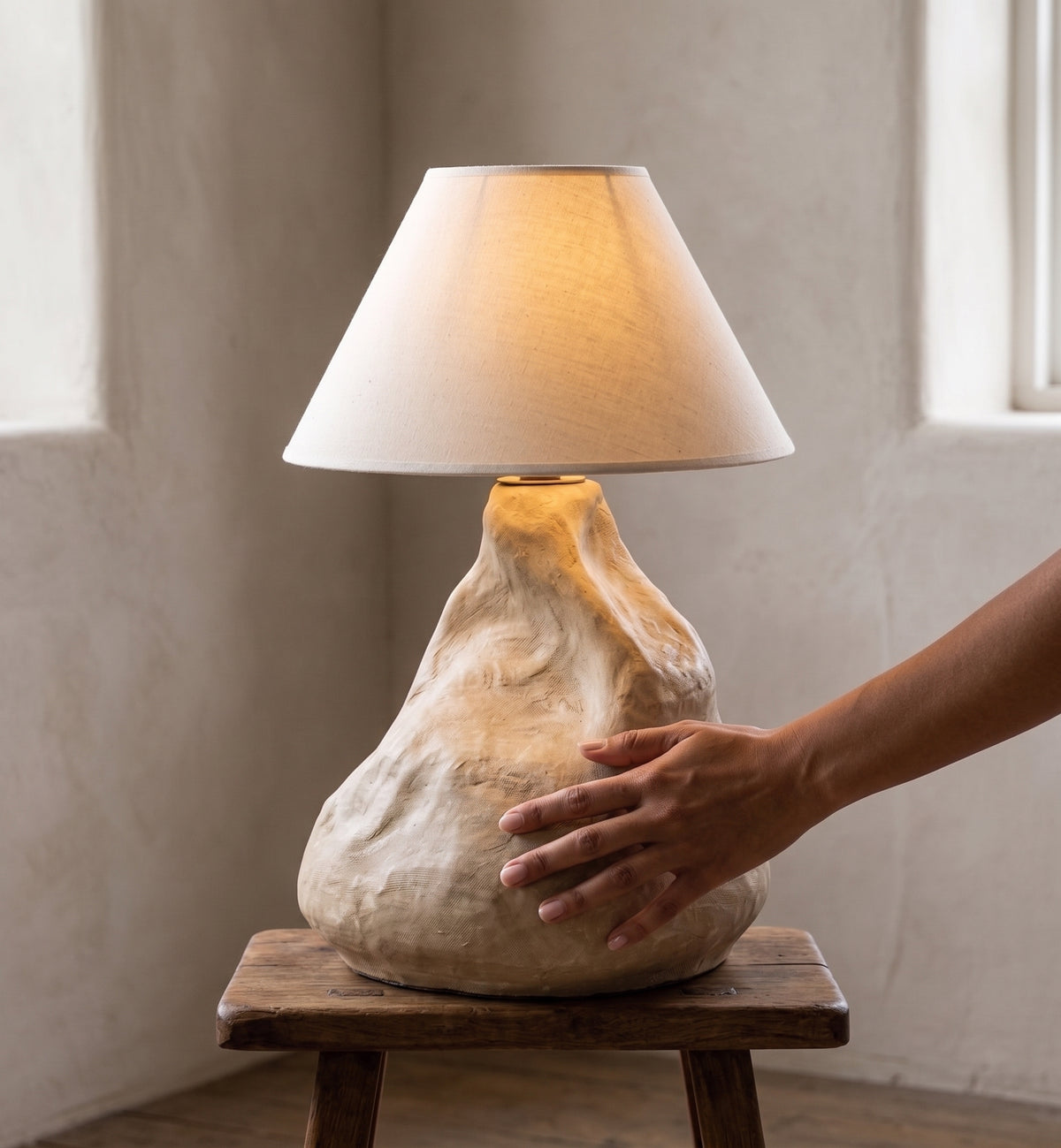 Handcrafted sculptural table lamp casting dramatic window shadow lines on a polished concrete floor
