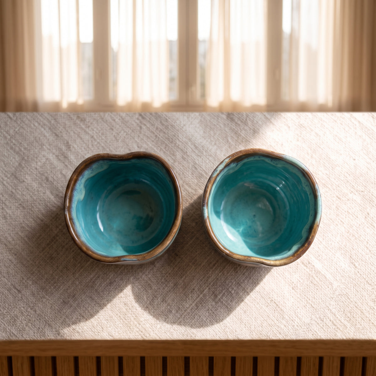 Top-down overhead view of two handmade ceramic shot glasses, showing the vibrant turquoise blue glaze on the interior and raw clay on the exterior.